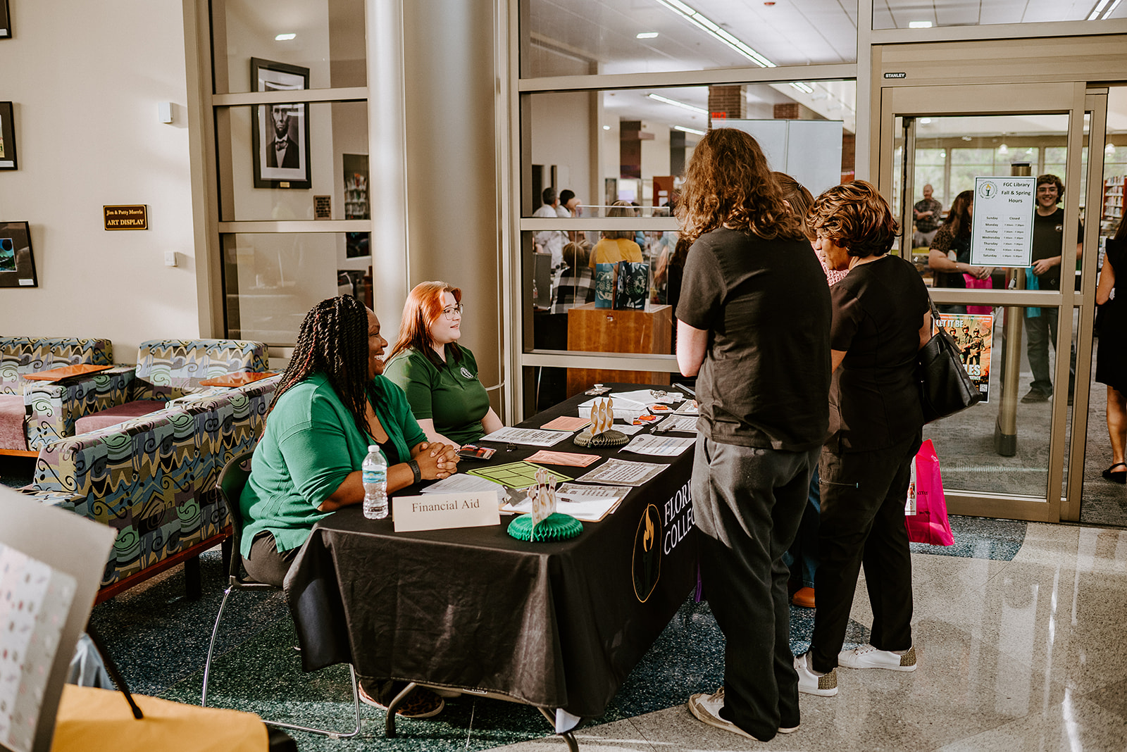 Two college employees assist visitors at a table during college event.