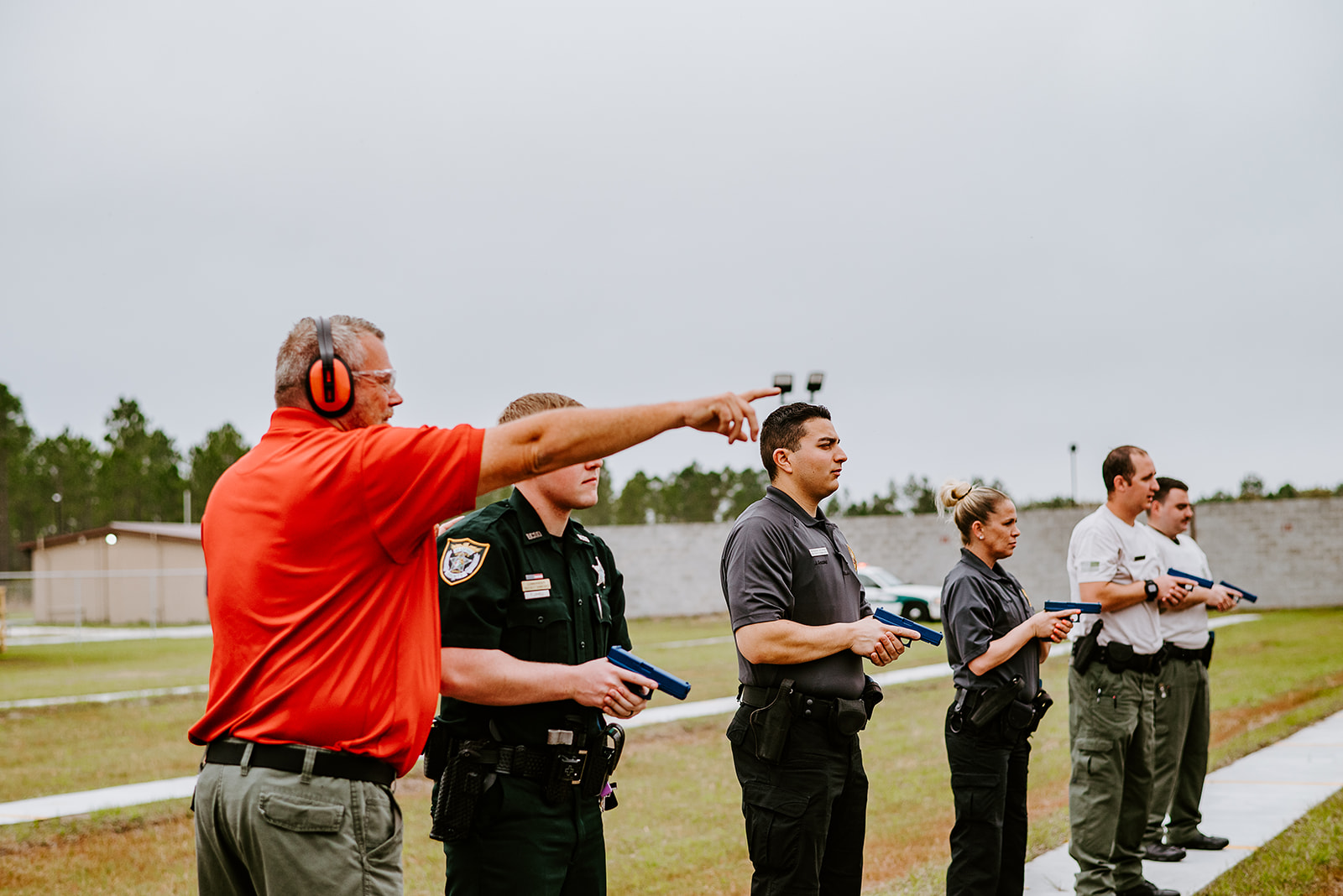 Instructor gives directions to a group of public safety trainees holding training pistols during an outdoor firearms training exercise.
